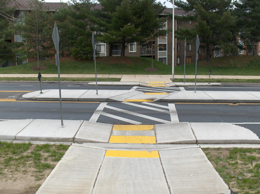 Photo shows the crosswalk, which extends straight across the street from the bulbout to the refuge island (one lane), then turns slightly to the right to cross the refuge island, then continues straight across the next lane to end at the bulbout (sidewalk extension) on the other side of the street.